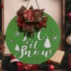 Let It Snow MDF wall plaque, 350 mm round green base with white lettering, snowflakes, trees & red festive ribbon bow