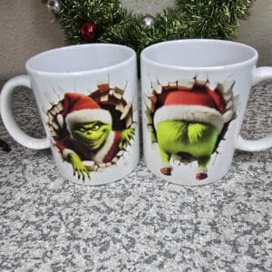 Two Grinch-themed Christmas mugs displayed on a countertop with festive holiday designs.
